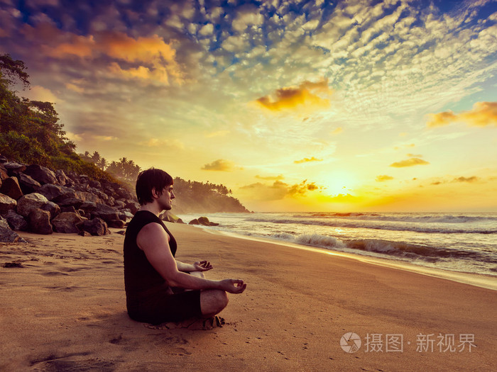 年轻的运动健身男子做瑜伽冥想在热带海滩上