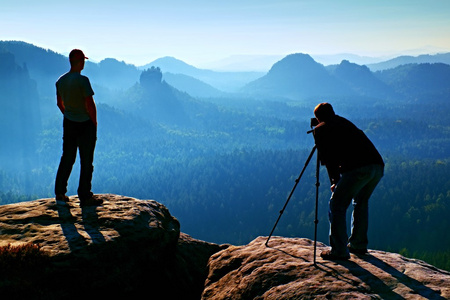 旅游指南和照片爱好者一起三脚架上悬崖和思维。在下面的美丽山谷梦幻般顽固景观，蓝色朦胧日出