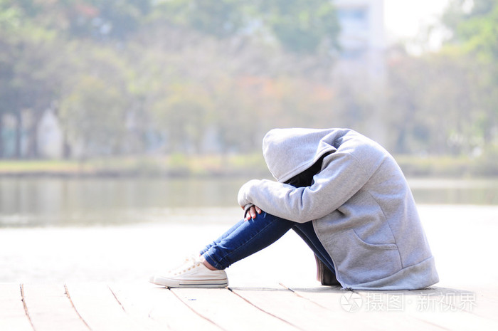 悲伤的女人抱着她坐在河边的膝盖