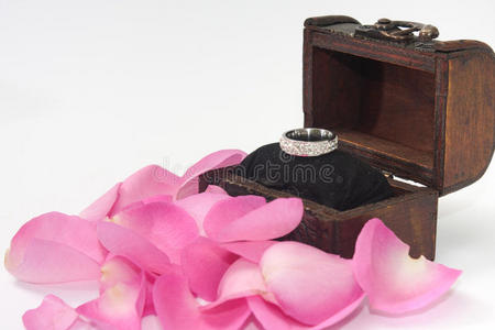 订婚戒指在木制胸部与粉红色玫瑰花瓣