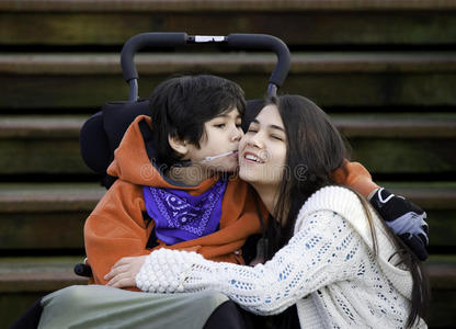 残疾的小男孩在坐着的时候亲吻他的姐姐的脸颊