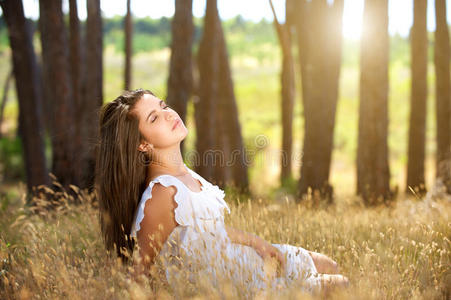 梦幻般的年轻女人坐在田野里，背景有阳光