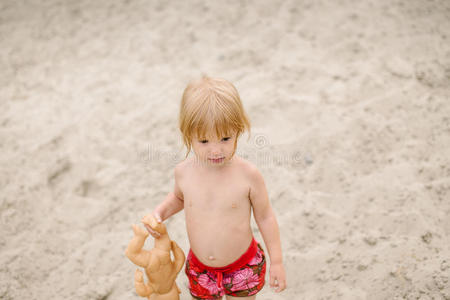 可爱的蹒跚学步的女孩在海滩上玩她的娃娃