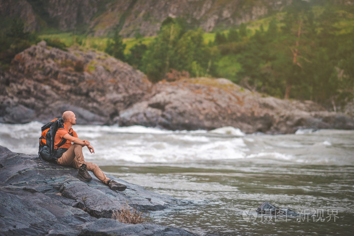 旅行者放松的男人坐在冰冷,美丽河附近的石头上.阿勒泰.俄罗斯