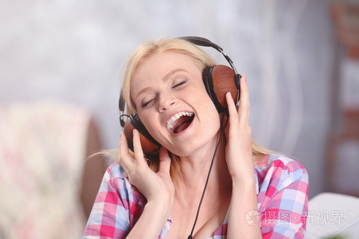 迷人的金发女孩,戴着耳机听音乐,在房间里唱歌