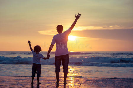 父亲和儿子在日落时在海滩上玩耍。
