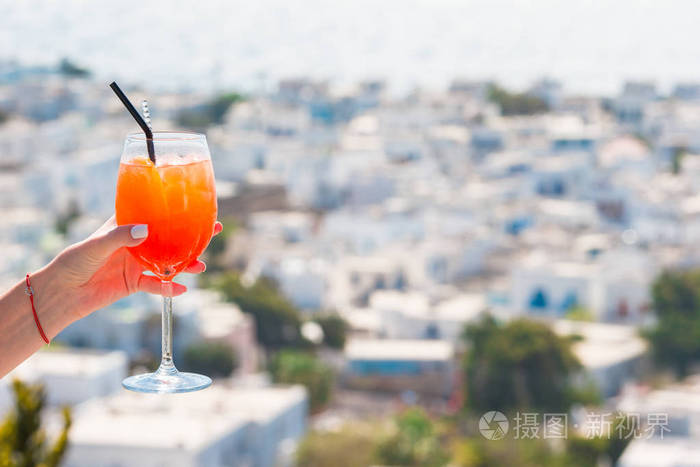 女手拿着玻璃喷 aperol 酒精饮料背景在美丽老米科诺斯岛希腊