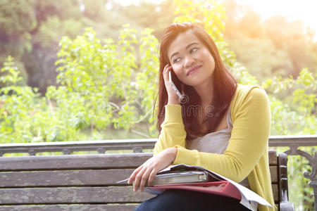 女大学生使用手机，坐在公园的木凳上。