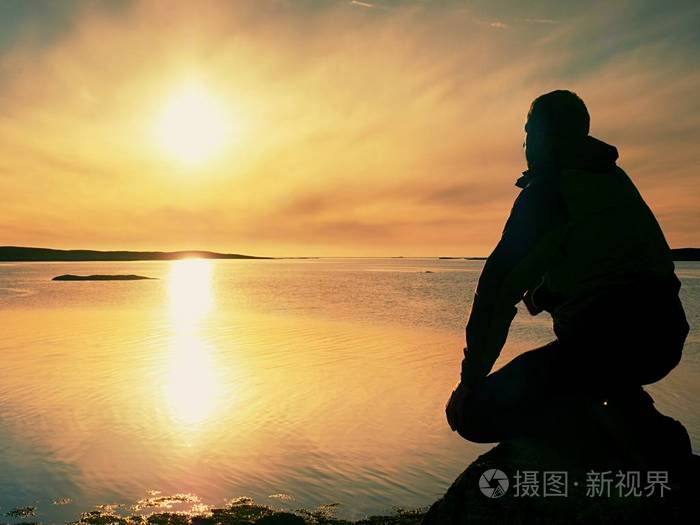 孤独的徒步旅行者独自一人坐在海边享受日落.查看岩石