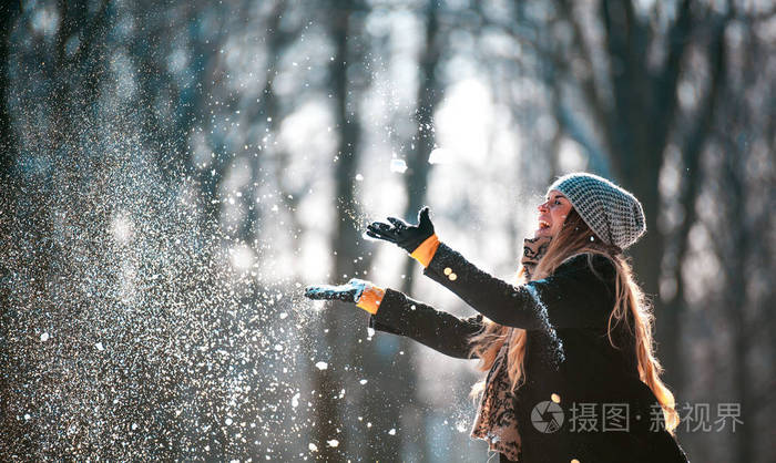 在阳光明媚的冬日微笑的年轻女子向空中撒雪