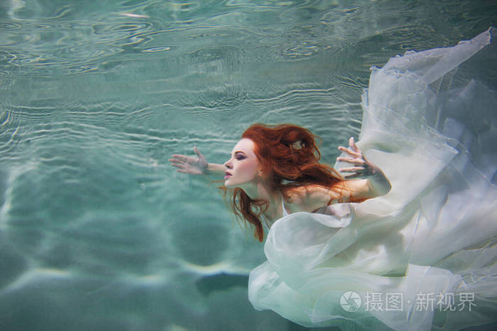 水下女孩.美丽的红头发的女人穿着白色的衣服 在水下游泳