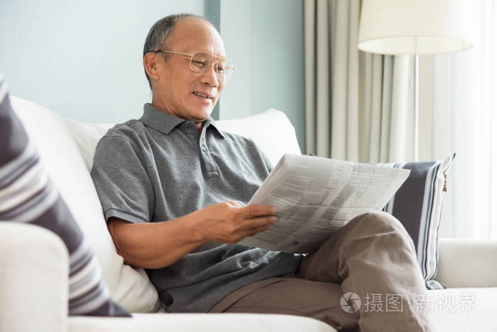 快乐的亚洲老人坐在家里看报纸轻松的微笑退休