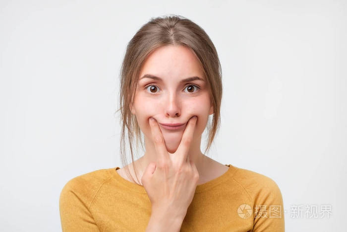 拍摄的美丽的白种少女女孩强迫微笑, 握住她的手指在她的嘴唇边缘