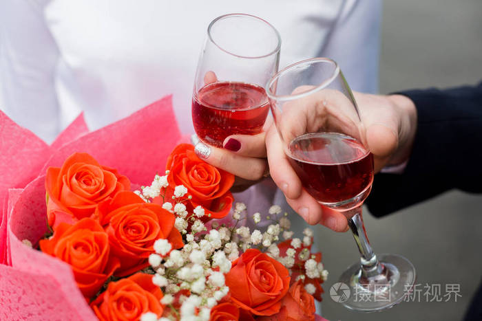 男人和女人的手拿着酒杯,在一束婚礼鲜花上放着红酒.