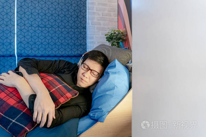 年轻的亚洲快乐男人睡在舒适的蓝色床上一边在卧室里