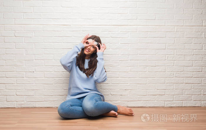 年轻的黑发女人坐在白色砖墙上的地板上,脸上洋溢着幸福的笑容,做着好