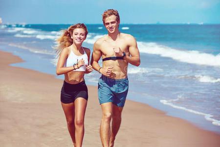 金发年轻夫妇在夏天在海滩上跑步