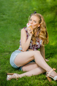 穿着短裤的金发女孩在户外草地上舔冰淇淋