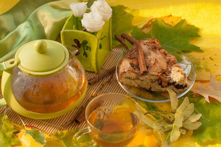 一个茶壶，一个盘子上的苹果自制馅饼，一杯新鲜的茶和秋天的叶子和花