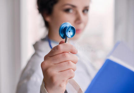 女性医生使用听诊器，文件夹站在窗口附近