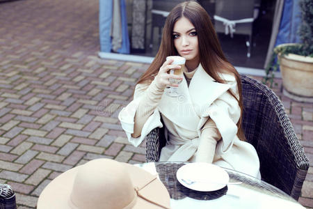 魅力女孩穿着豪华的米色外套喝咖啡