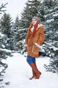 冬天公园里的女孩在白天。 有雪的冷杉树。 红头发女人的全长。