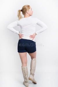 漂亮的年轻金发女郎穿着白色衬衫，蓝色短裤和高靴摆姿势