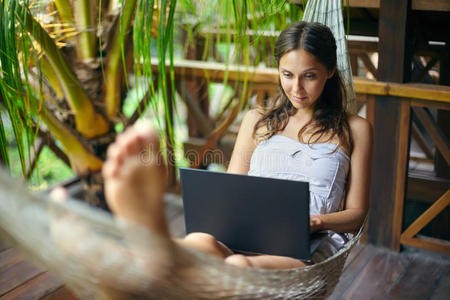 美丽的女人躺在吊床上，带着笔记本电脑在热带地区