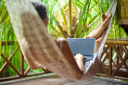 美丽的女人躺在吊床上，带着笔记本电脑在热带地区