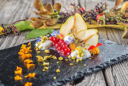 独家秋季奶油甜点与梨，醋栗和开心果在黑板上，装饰鲜花花瓣，产品
