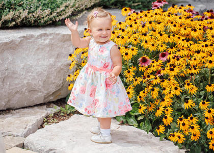 可爱的白色白种人女婴穿着白色连衣裙站在花园公园外面的黄色花朵之间