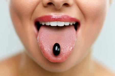 美丽的女人嘴上有药丸在舌头上。 吃药的女孩