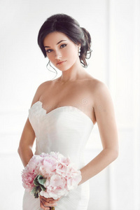 美丽的黑发女人作为新娘，粉红色的婚礼花束在白色