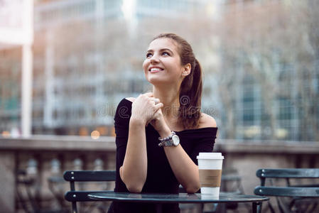 美丽快乐的女商人在午餐时间坐在城市公园，或者用纸咖啡杯喝咖啡休息。
