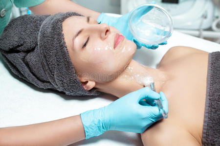 美容师在水疗沙龙中为美丽的年轻女性涂上带刷子的面膜。 化妆品程序皮肤护理。
