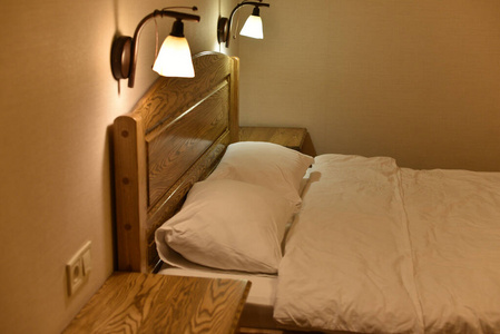 旅馆房间里的床。床和枕头。一张有木制床头板两个橱柜和落地灯的床。