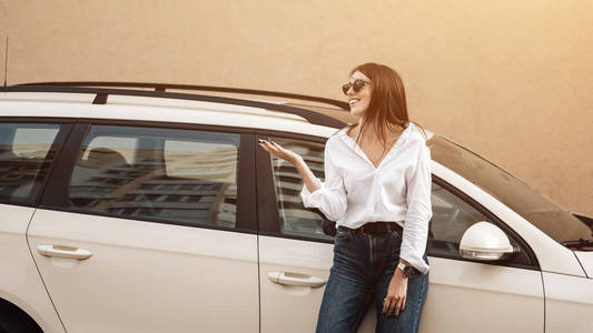 一位穿着牛仔裤和白衬衫的时尚年轻女性在汽车附近摆姿势的特写镜头，商务小姐，女性权力概念