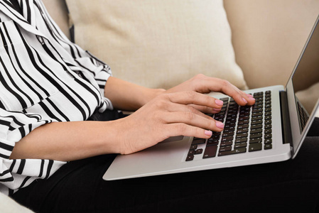 女人坐在沙发上用笔记本电脑工作，特写