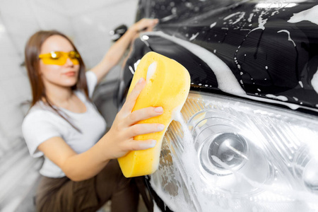 工人美女用黄色海绵清洗汽车黑色泡沫。洗车服务