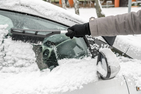 女人用刷子把汽车从雪地上擦下来。冬季冰雪寒冷天气下人们的交通理念。