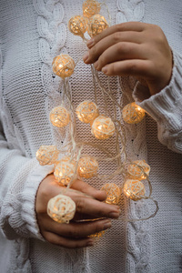 掌心的光。女性手拿着一个有柳条圆球的花环。身穿白色毛衣的女孩手里拿着圣诞灯，温暖的新年心情，柔情似水