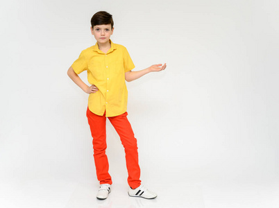 青少年表现出男生的情感。摄影棚里一个穿着红色裤子和黄色衬衫的孩子在白色背景下的全幅照片。以各种姿势站在摄像机前。
