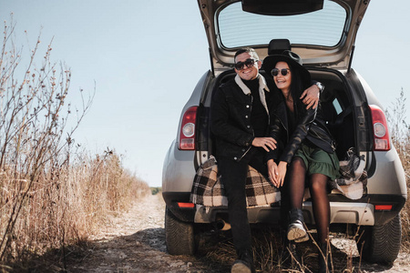 一对快乐的旅行情侣穿着黑色时尚的衣服，在田野路上享受汽车旅行，度假的概念
