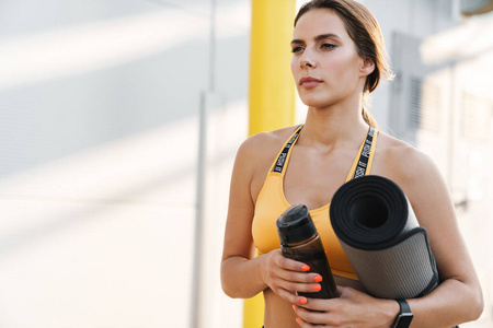 Image of beautiful woman walking with yoga mat and water bottle 