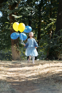 小可爱的女孩拿着一堆气球在公园里跑。她笑得很挑逗。快乐童年的概念。