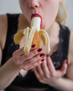 那个穿着黑色蕾丝内衣的金发女郎性感地吃着香蕉。性感的红唇美女性感地吮吸和舔香蕉。口头上的愉悦。闭合。