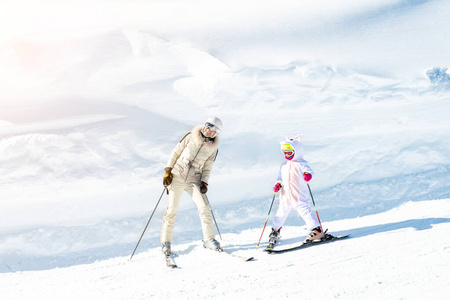 年轻的成年漂亮的运动型母亲与小女儿在高山滑雪胜地滑雪。苗条的妈妈穿着豪华时尚滑雪服，孩子们享受户外娱乐活动