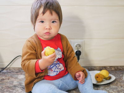 小孩吃梨。一个吃水果的小男孩。在厨房里。
