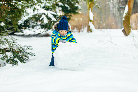 可爱的小男孩在堆雪人。滚大雪球