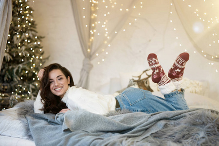 年轻美丽的微笑女子穿着圣诞毛衣和袜子，在一个装饰的房间里庆祝新年和圣诞节的喜庆气氛